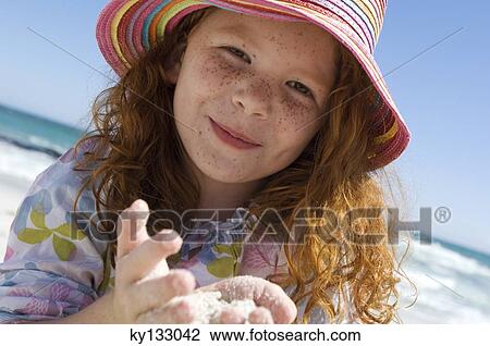 Stock Image - Portrait of a little girl smiling looking at the camera, sand in her hands, outdoors. Fotosearch