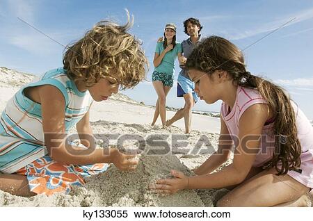 Stock Photography - Two children playing on the beach, parents in background, outdoors. Fotosearch
