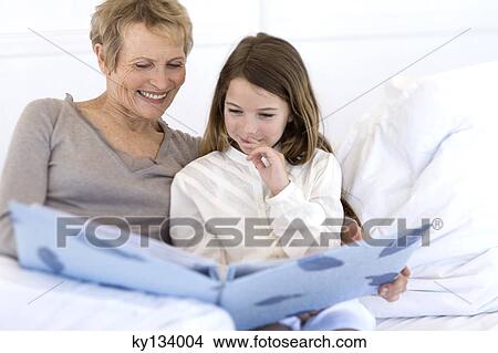 Senior woman and little girl in bed, looking at photograph album View Large Photo Image Picture - Senior woman and little girl in bed, looking at photograph album. Fotosearch