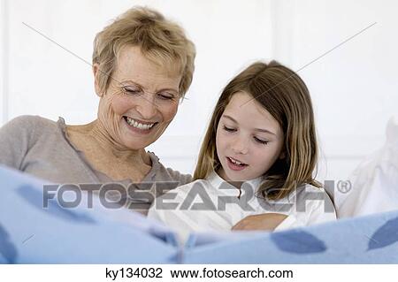 Stock Image - Senior woman and little girl in bed, looking at photograph album. Fotosearch