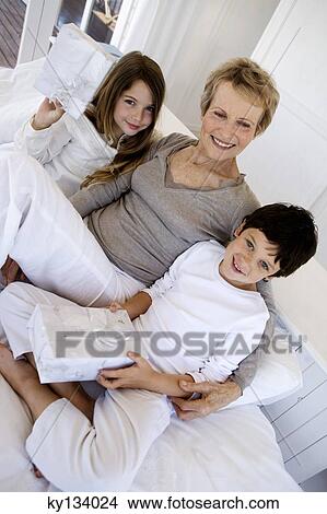 Picture - Senior woman and two children holding gifts, indoors. Fotosearch