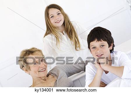 Stock Image - Senior woman and two children smiling for the camera, indoors. Fotosearch