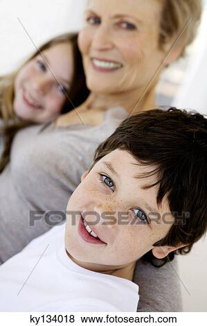 Stock Photo - Senior woman and two children smiling for the camera, indoors. Fotosearch