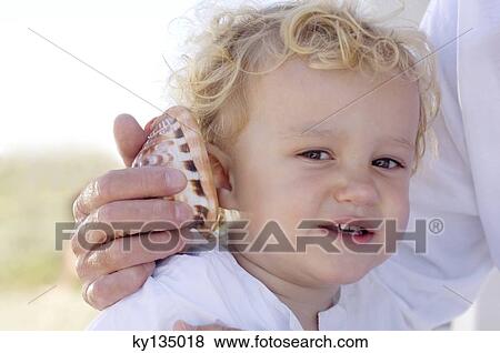 Stock Photo - Portrait of a little boy with a shell against his ear. Fotosearch