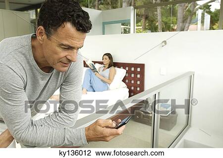 Couple in bedroom, man looking his cell, woman reading magazine, indoors View Large Photo Image Stock Image - Couple in bedroom, man looking his cell, woman reading magazine, indoors. Fotosearch