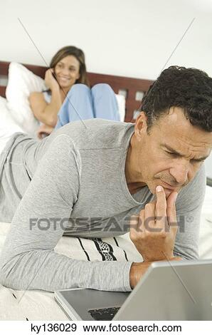 Couple in bedroom, man using laptop, indoors View Large Photo Image Stock Photo - Couple in bedroom, man using laptop, indoors. Fotosearch