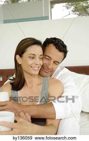 Couple sitting on bed, indoors View Large Photo Image Stock Photo - Couple sitting on bed, indoors. Fotosearch
