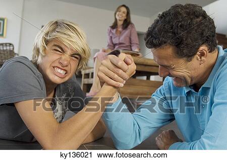 Father and son arm-wrestling indoors, mother in background View Large Photo Image Stock Image - Father and son arm-wrestling indoors, mother in background. Fotosearch