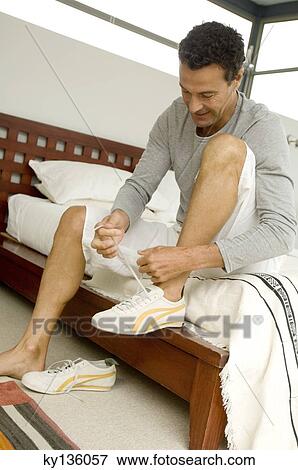 Man sitting on bed, tiying his baskets, indoors View Large Photo Image Stock Photo - Man sitting on bed, tiying his baskets, indoors. Fotosearch
