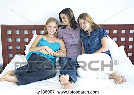 Mother and two teenagers sitting on a bed, indoors View Large Photo Image Stock Photo - Mother and two teenagers sitting on a bed, indoors. Fotosearch