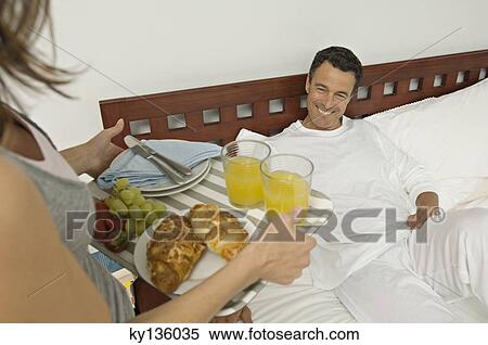 Woman bringing breakfast to man lying on bed, indoors View Large Photo Image Stock Photography - Woman bringing breakfast to man lying on bed, indoors. Fotosearch