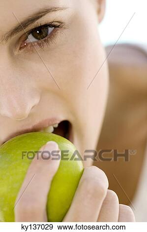 Stock Photo - Portrait of a young woman eating an apple, indoors. Fotosearch
