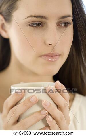 Stock Image - Portrait of a young woman holding a cup, indoors. Fotosearch