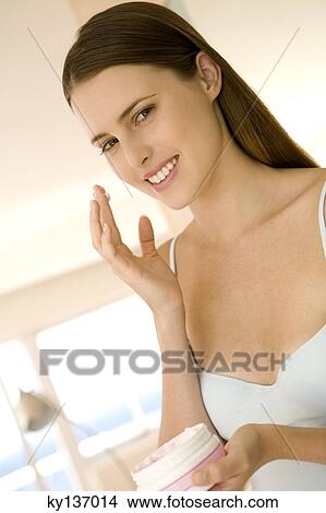 Portrait of a young woman holding moisturizer, indoors View Large Photo Image Picture - Portrait of a young woman holding moisturizer, indoors. Fotosearch