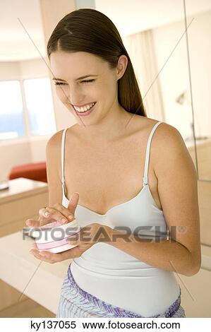 Stock Photography - Portrait of a young woman holding moisturizer, indoors. Fotosearch