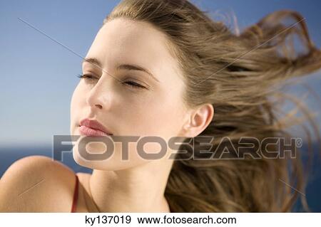 Stock Photo - Portrait of a young woman looking away, wind in her hair, outdoors. Fotosearch