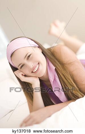 Portrait of a young woman smiling, lying in front, indoors View Large Photo Image Stock Photo - Portrait of a young woman smiling, lying in front, indoors. Fotosearch