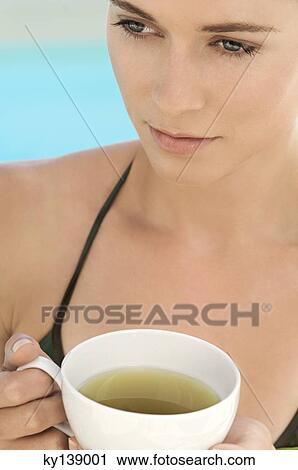 Stock Image - Portrait of young woman holding a cup of green tea, outdoors. Fotosearch