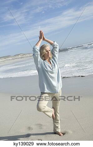 Stock Photo - Woman in yoga attitude on the beach, outdoors. Fotosearch