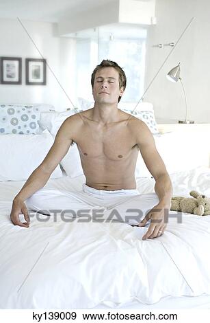 Stock Photo - Young man in yoga attitude, indoors. Fotosearch