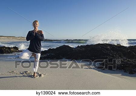 Picture - Young woman in yoga attitude on the beach, outdoors. Fotosearch