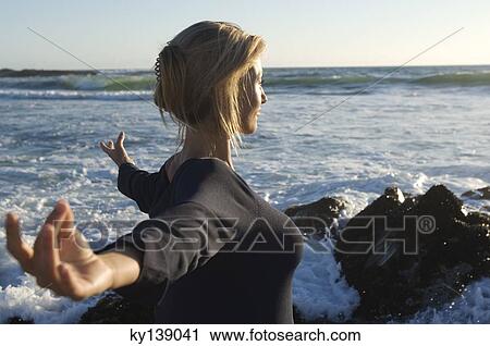 Stock Image - Young woman in yoga attitude on the beach, outdoors. Fotosearch