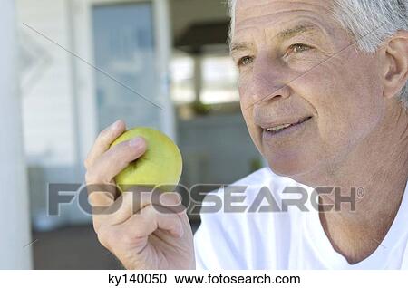 Stock Image - Portrait of a senior man holding an apple. Fotosearch