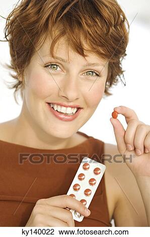Stock Image - Portrait of a young smiling woman holding pills. Fotosearch