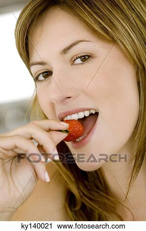 Stock Image - Portrait of a young woman eating a strawberry. Fotosearch