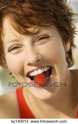 Portrait of a young woman holding strawberry between her teeth View Large Photo Image Stock Image - Portrait of a young woman holding strawberry between her teeth. Fotosearch