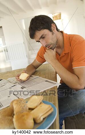 Young man reading newspaper, breads in foreground View Large Photo Image Stock Image - Young man reading newspaper, breads in foreground. Fotosearch