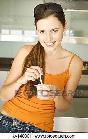 Stock Image - Young smiling woman eating yogurt. Fotosearch