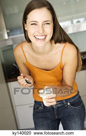 Stock Image - Young smiling woman eating yogurt. Fotosearch