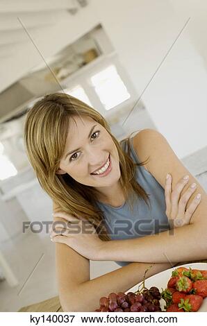 Stock Photo - Young smiling woman looking at camera, strawberries and grapes in foreground. Fotosearch