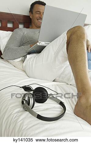 Man lying on bed, using laptop View Large Photo Image Stock Photography - Man lying on bed, using laptop. Fotosearch