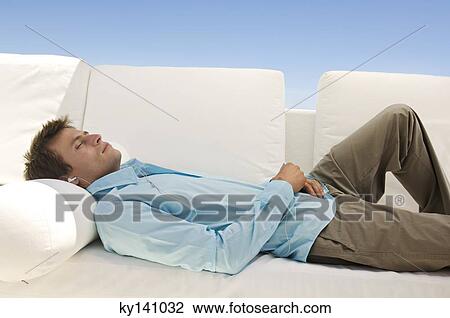 Young man listening to MP3 player lying on sofa View Large Photo Image Stock Image - Young man listening to MP3 player lying on sofa. Fotosearch