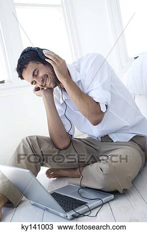 Stock Image - Young man listening to music with laptop. Fotosearch