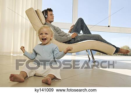 Young man listening to music with headphones, smiling little girl in foreground View Large Photo Image Stock Photo - Young man listening to music with headphones, smiling little girl in foreground. Fotosearch