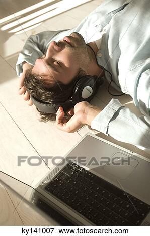 Young man lying on floor, listening to music with laptop View Large Photo Image Stock Photo - Young man lying on floor, listening to music with laptop. Fotosearch
