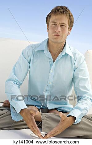 Young man sitting cross-legged listening to MP3 player View Large Photo Image Picture - Young man sitting cross-legged listening to MP3 player. Fotosearch