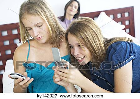 2 smiling teenage girls using mobile phones, woman in background View Large Photo Image Stock Photo - 2 smiling teenage girls using mobile phones, woman in background. Fotosearch