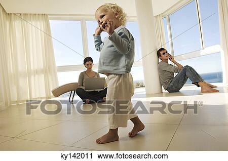 Stock Image - Little girl using mobile phone, parents in background. Fotosearch