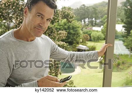 Man leaning against bay window, holding mobile phone View Large Photo Image Stock Image - Man leaning against bay window, holding mobile phone. Fotosearch