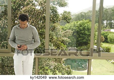 Man leaning against bay window, using mobile phone View Large Photo Image Stock Photo - Man leaning against bay window, using mobile phone. Fotosearch