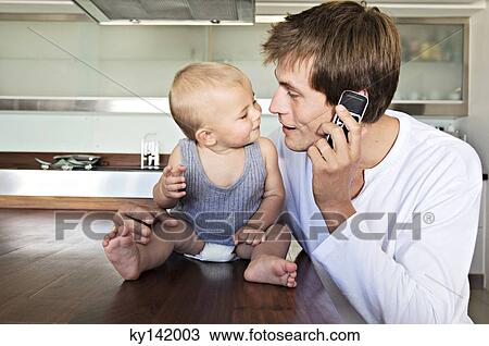 Young man phoning, embracing baby View Large Photo Image Stock Image - Young man phoning, embracing baby. Fotosearch