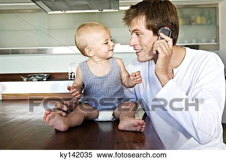 Young man phoning, embracing baby View Large Photo Image Stock Photography - Young man phoning, embracing baby. Fotosearch