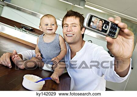 Young man with baby, using camera phone View Large Photo Image Stock Photo - Young man with baby, using camera phone. Fotosearch