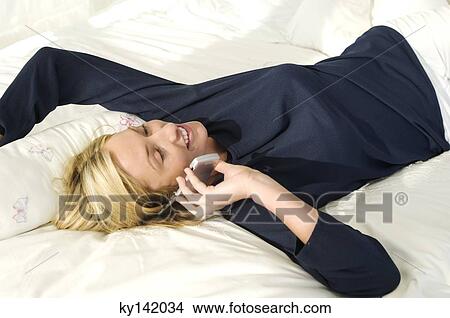 Young woman lying on bed, using mobile phone View Large Photo Image Picture - Young woman lying on bed, using mobile phone. Fotosearch