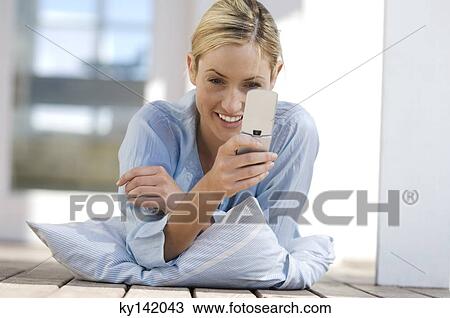 Young woman lying on floor, using mobile phone View Large Photo Image Stock Image - Young woman lying on floor, using mobile phone. Fotosearch