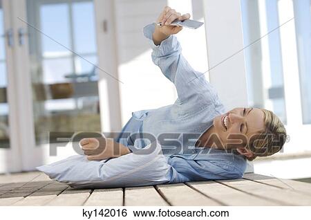 Stock Photograph - Young woman lying on floor, using mobile phone. Fotosearch